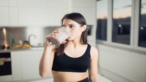Moça tomando whey protein na cozinha