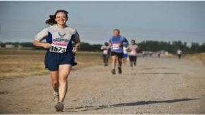 Mulher em prova de corrida, correndo em rua sorrindo, ao fundo homens correndo